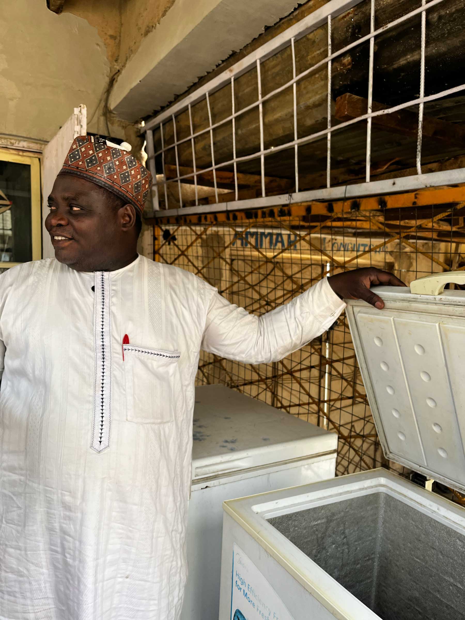Alheji Gembo showing off one of the refrigerators that he sells cold drinks out of