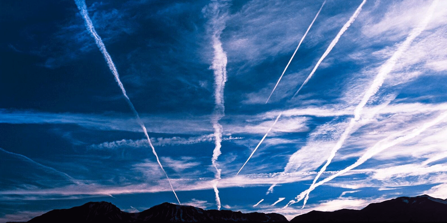 Contrails streak across a blue sky with mountains in the foreground